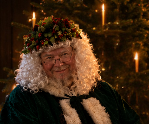 father christmas in green outfit surrounded by candles and greenery
